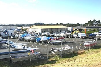 Boat storage yard at Holiday Outboards with numerous boats on trailers under blue tarps